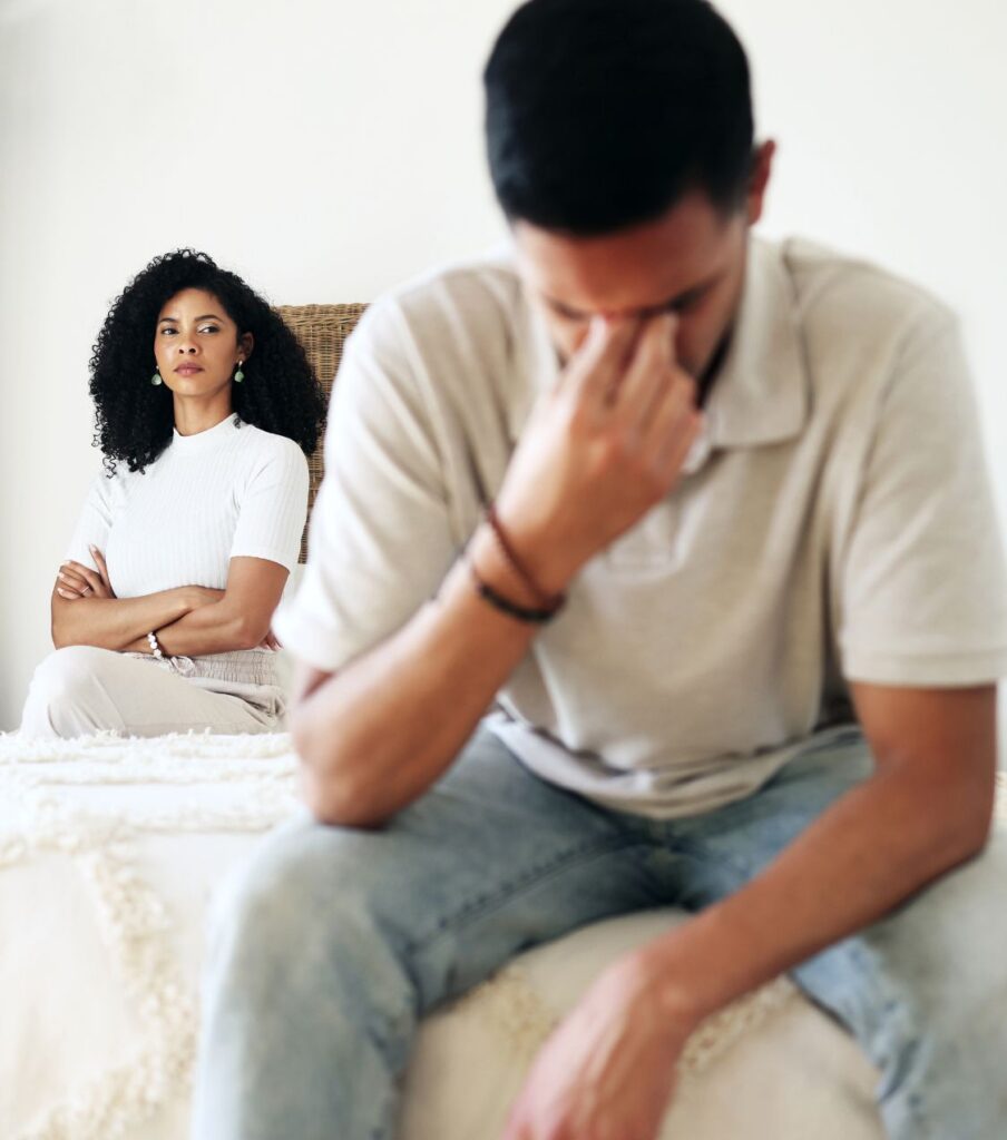 Man sitting on the bed covering his eyes looking apologetic while wife is sitting behind him looking upset. You may be struggling with the aftermath of infidelity feeling stuck and unable to heal. You can survive infidelity and rebuild your marriage with Affair Recovery Program by relationship Experts Online in the United States, Canada, and worldwide. 