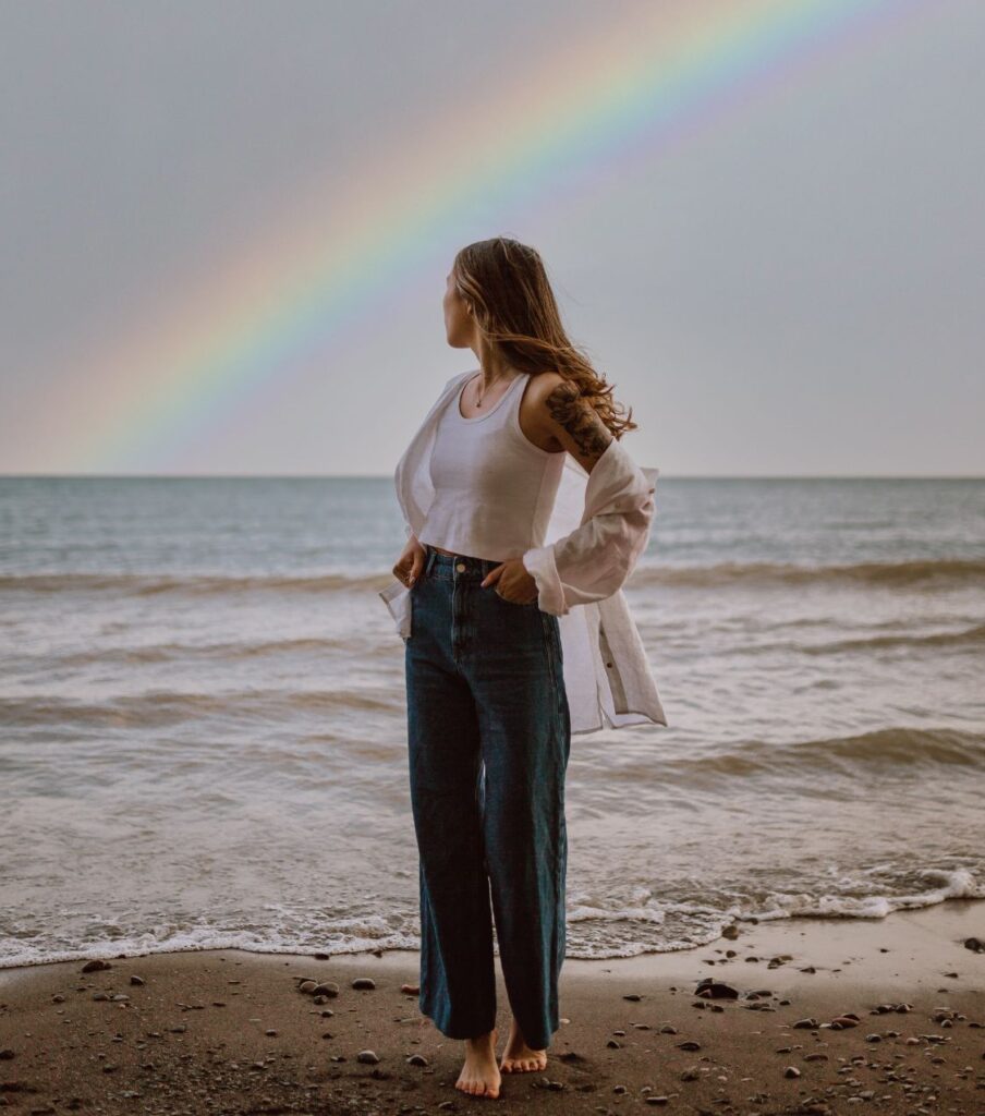 A woman watching a rainbow in the beach. She knows affair recovery takes time to heal but she is moving forward. To start affair recovery book a free consultation with Relationship Experts Online now!