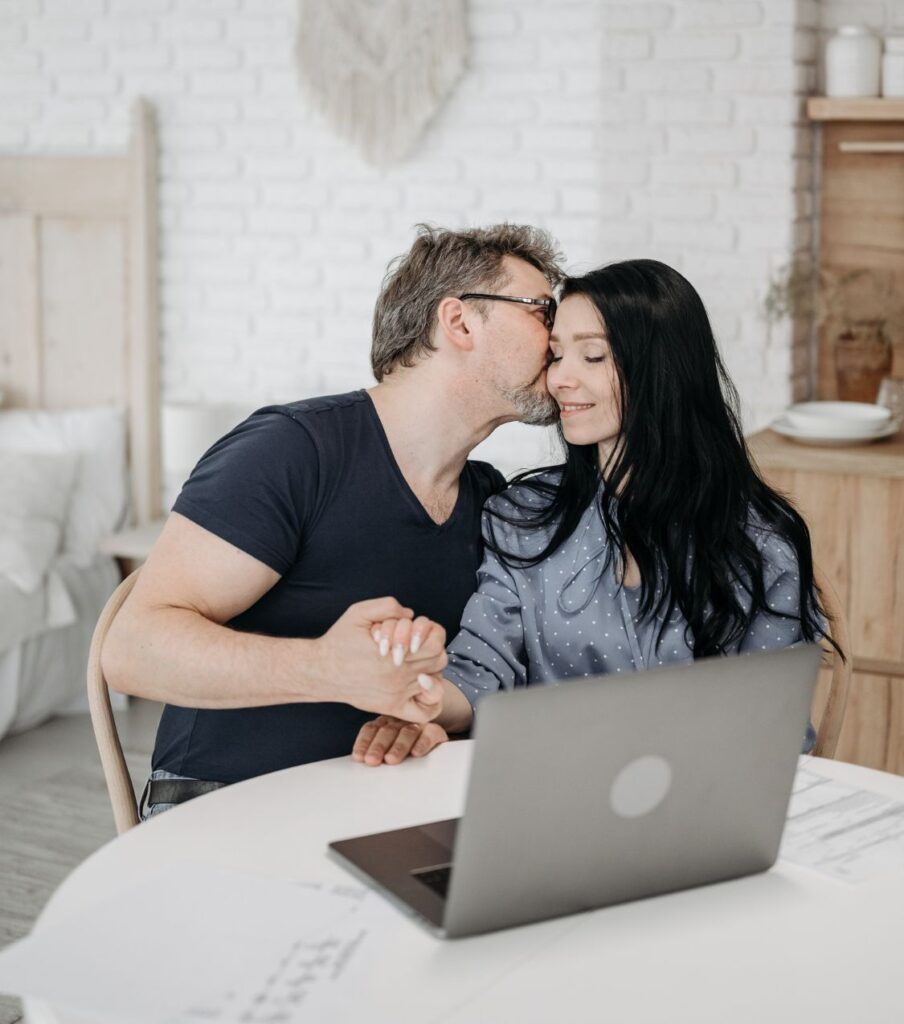 A couple sitting in front of a laptop looking  happy to have a plan for recovering after infidelity. If you need a roadmap to healing after an affair than check out affair recovery coaching programs by Relationship Experts Online. 
