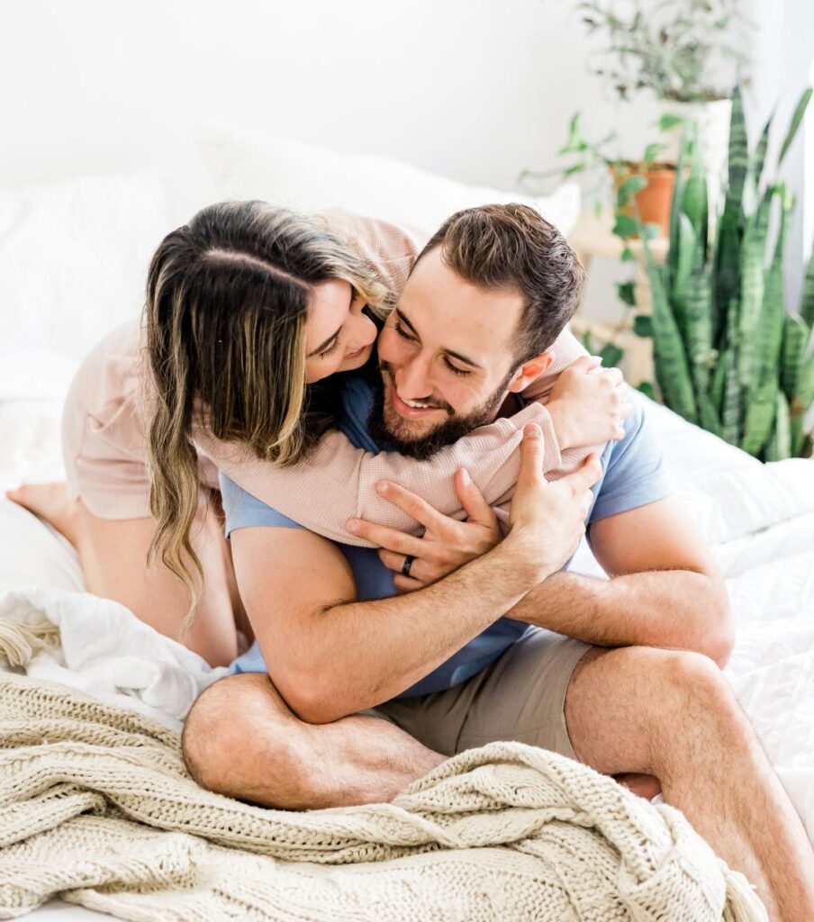 A happy woman is hugging her husband on a bed. They are happy to have an affair recovery healing program. If you are in the aftermath of an affair we can help your healing get on track. Learn more about Relationship Experts Online affair recovery program. 