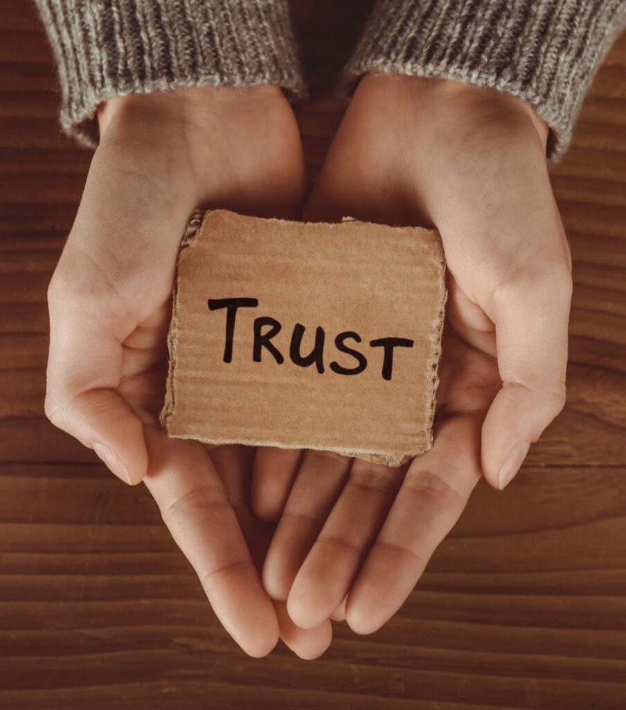 In the palm of two hands rests a note labeled 'Trust,' symbolizing the crucial journey to earn trust when both partners are uncertain about how to initiate healing after infidelity. Seek the support you need from Relationship Experts based in Florida, USA.