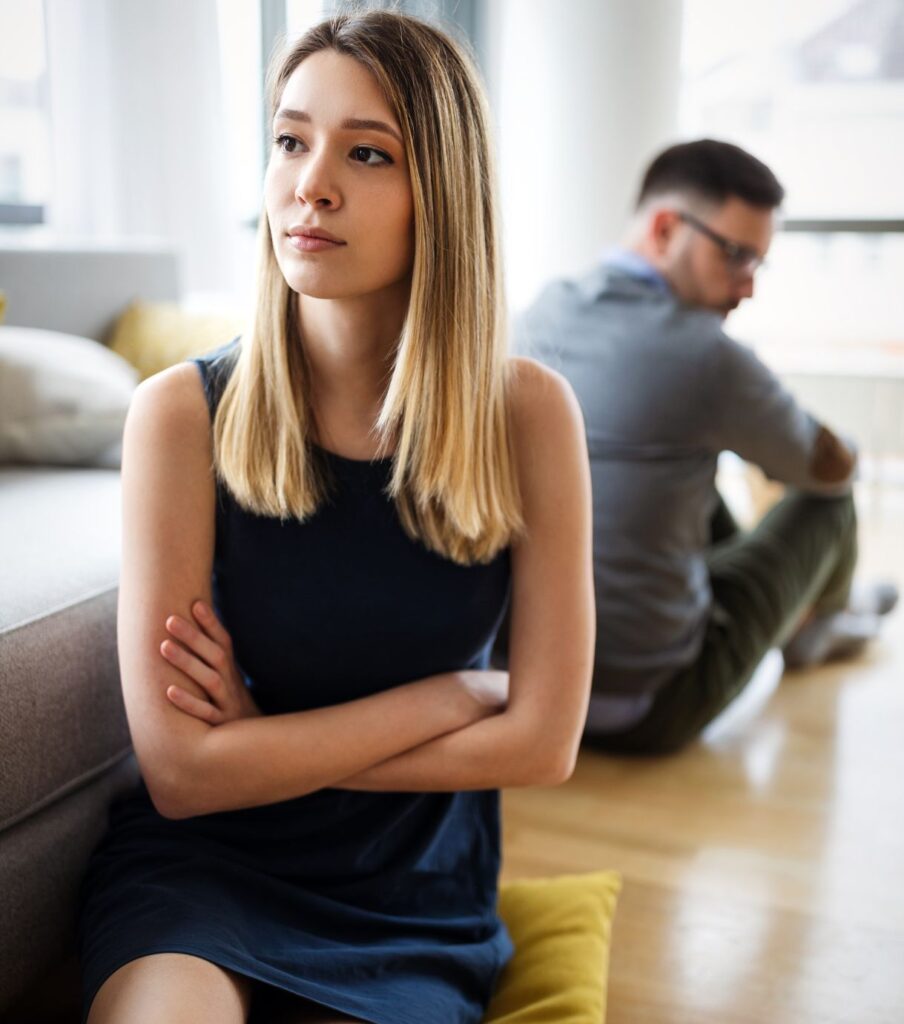 A couple sitting on the floor, back to back. They look distanced and lost after an affair. If you want to know how to help your spouse heal from your affair in the USA & Canada, you can schedule a free consultation with Relationship Experts.