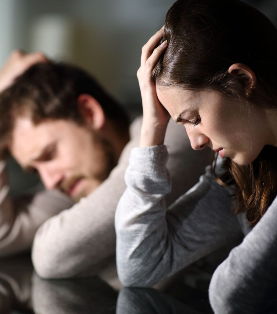 A distressed couple leaning on their hands, navigating the emotional aftermath of an affair. Discover the healing power of an effective affair recovery program to save your relationship. Offering counseling services in the United States, Canada, United Kingdom, New York, Ohio, Florida, California, North Carolina, and Colorado. Call us today to begin your journey toward healing!