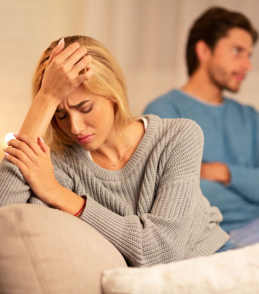 A frustrated woman sits on a sofa with her spouse looking away, highlighting the challenges of marriage reconciliation. Relationship Experts Online helps couples in North Carolina, the USA, Australia, Canada, and the United Kingdom.