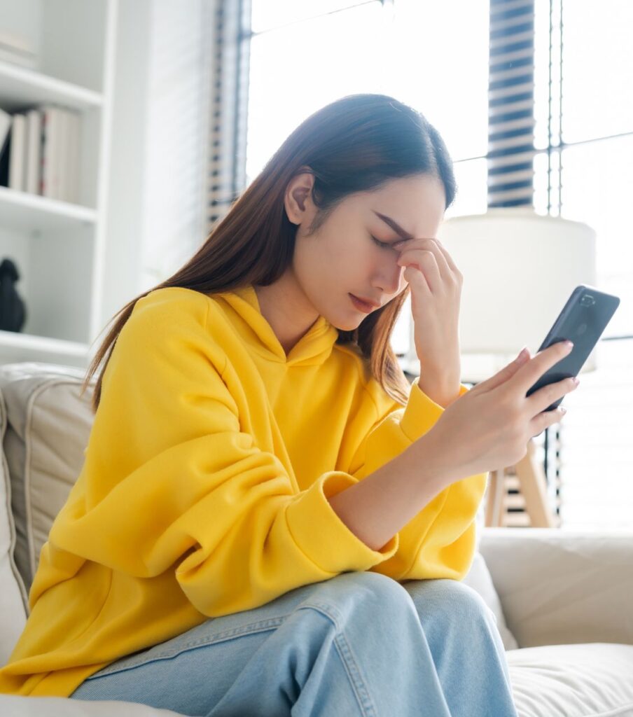 A woman sits holding her phone and covering her eyes, showing the emotional struggle of marriage reconciliation. Schedule a free phone consultation with Relationship Experts for guidance on reconciliation after infidelity. Available in New York, the US, Canada, and the UK.