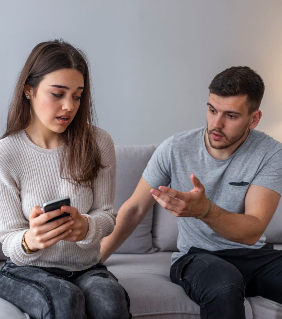 A woman hides her cell phone from a man, illustrating trust issues in Post Traumatic Infidelity Syndrome. Schedule a consultation with our therapists in Florida, New York, California and the US.

