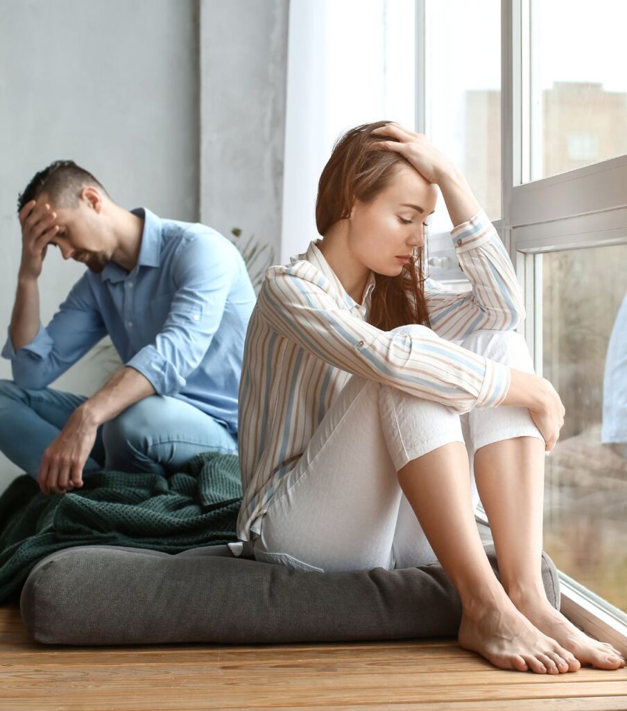 A couple sits back-to-back, holding their foreheads, representing Post Traumatic Infidelity Syndrome a couple is going through. Schedule a free consultation with Relationship Experts LLC to get the help from the experts in New York, California, Florida and in the United States.