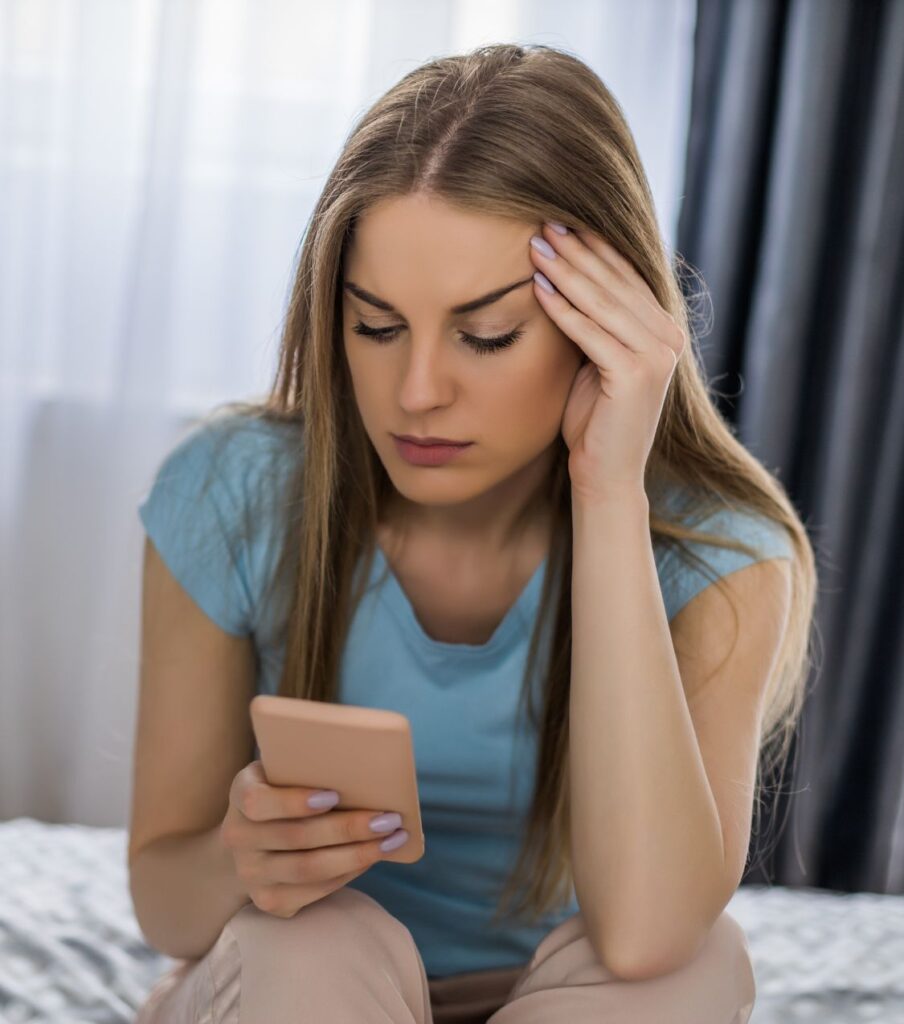 A woman looks at her phone, illustrating how small events, like a missed call, can trigger betrayal reminders. Complete your affair recovery with expert help in the USA and globally