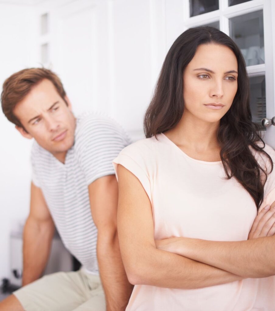 A woman crosses her arms with her back to a man, symbolizing the emotional struggle of surviving infidelity. Relationship experts guide couples in the United States and worldwide toward healing and reconnection.