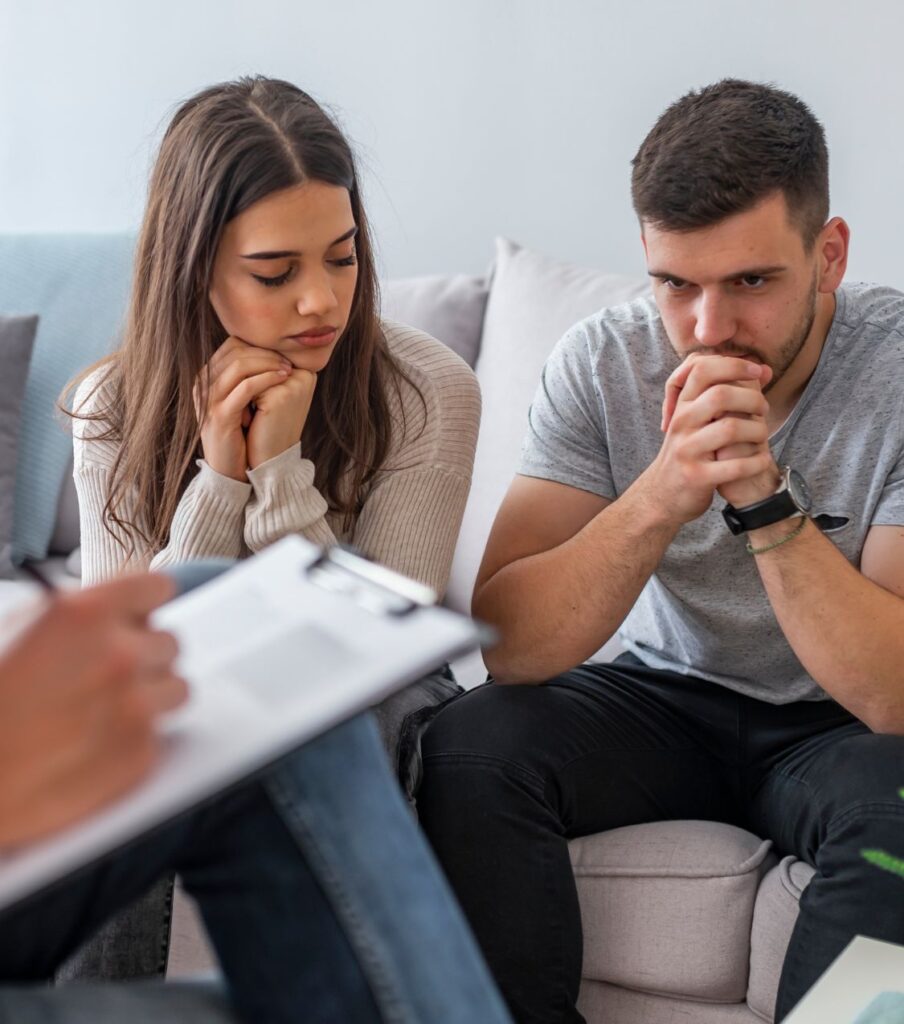 Man and woman sitting with heads in hands | Survive infidelity in the USA | Forgiveness in the United States | Canada | The United Kingdom Man and woman sitting with heads in hands during a therapy session, seeking guidance on how to survive infidelity and move beyond forgiveness. Relationship experts in the USA, Canada, and United Kingdom offer support for couples rebuilding trust.