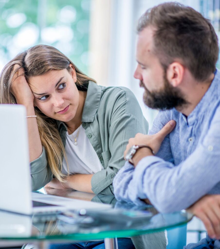 A couple sits leaning on a table, looking at each other, symbolizing progress in healing after cheating. Our therapists help couples in the United States, Canada, the United Kingdom, and worldwide rebuild trust and save their relationship. Call us today.