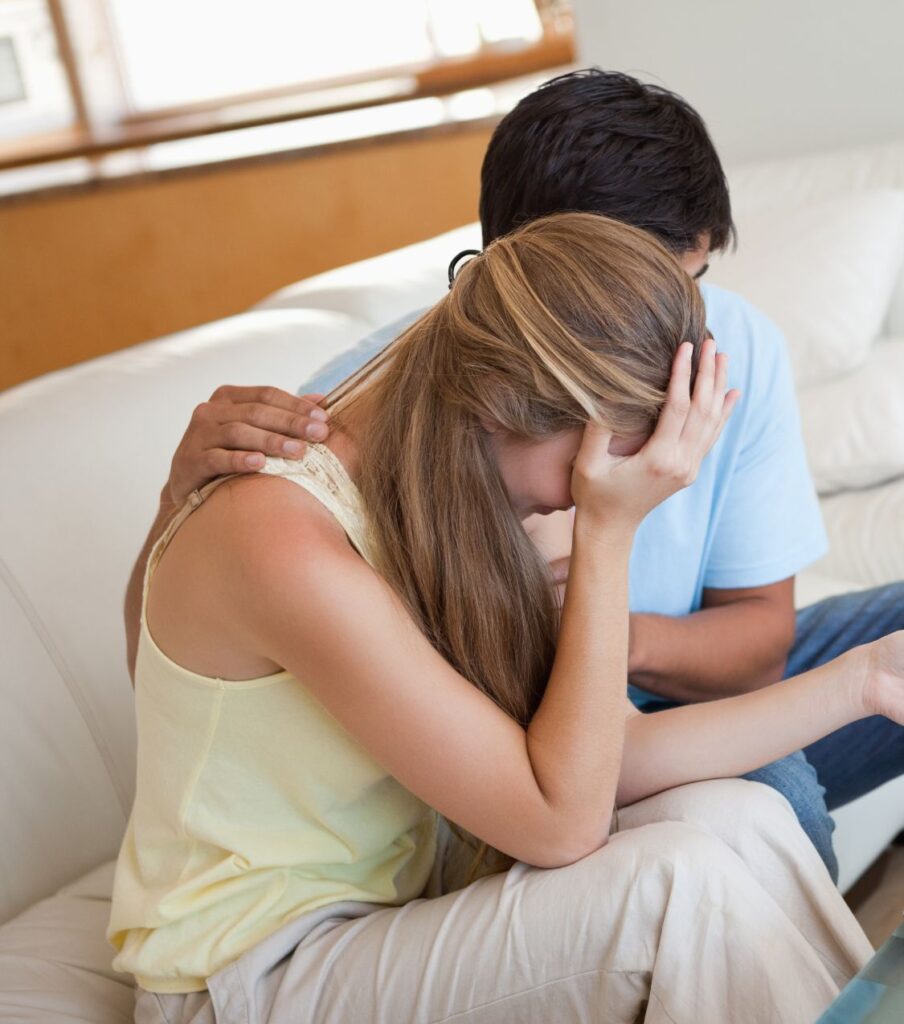 A man hugs a crying woman after infidelity. Couples who follow the three stages of healing after infidelity can recover faster. Get expert guidance in the United States, Canada, the UK, and globally. Schedule a free consultation today.
