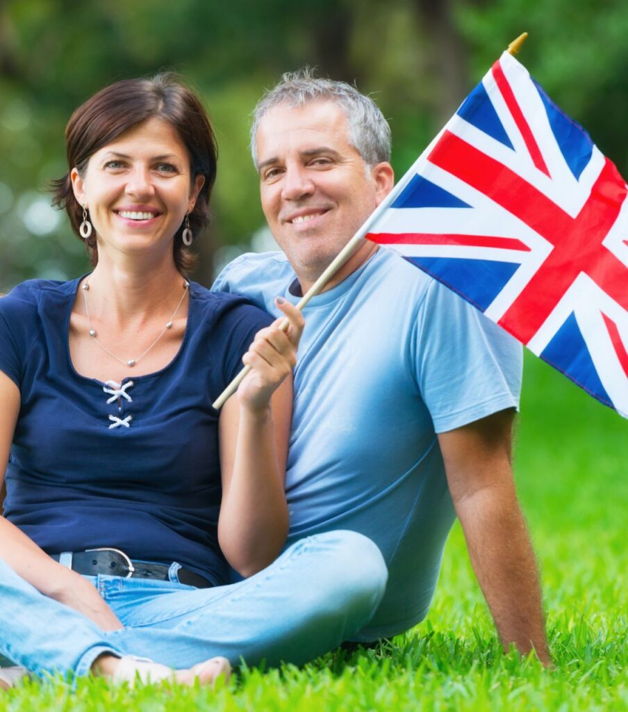 A smiling British couple sitting together on grass holding a Union Jack flag, representing hope and reconnection after choosing real expertise over quick fixes for affair recovery. Helping couples worldwide to heal after infidelity in marriage with a structured, private program. Book your confidential consultation now at relationshipexpertsonline.com