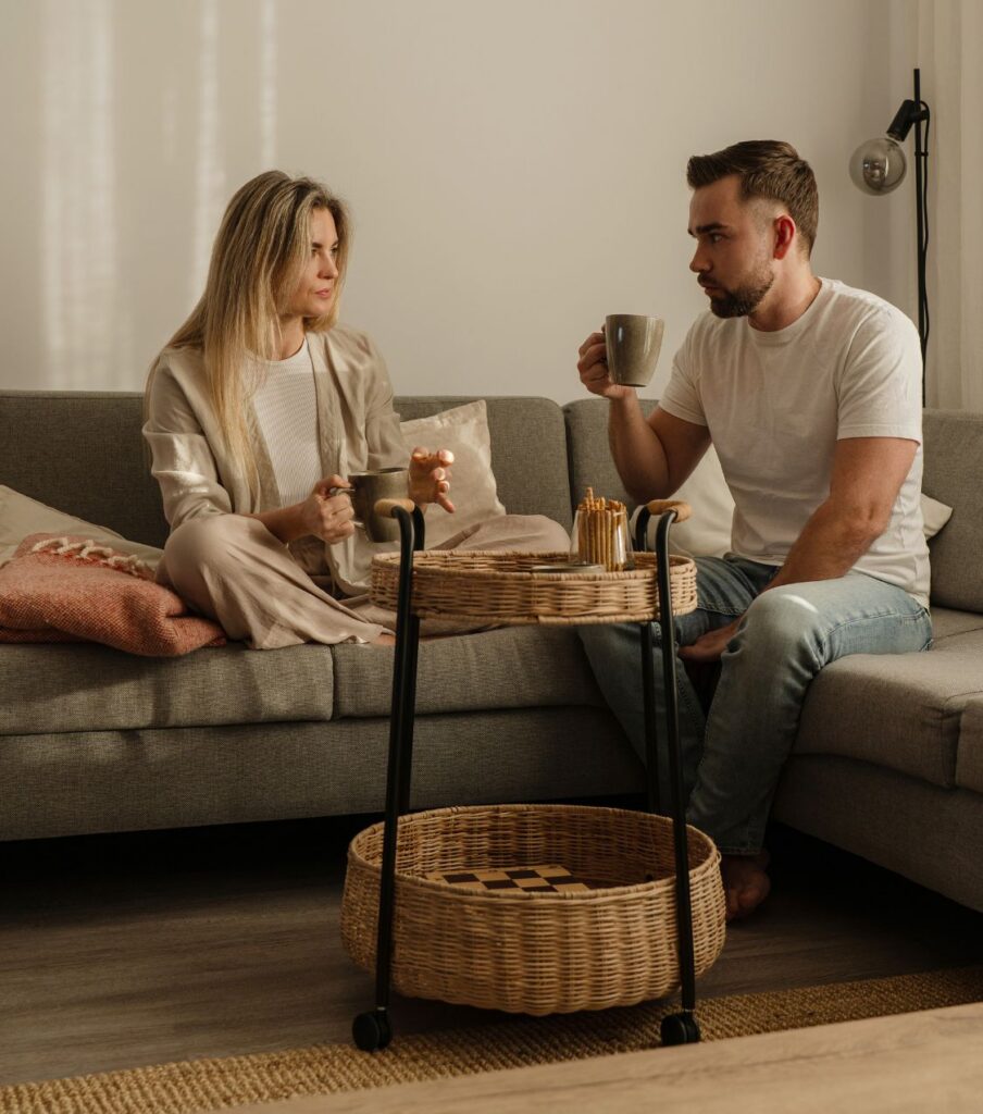 A man and woman sit on a couch having a serious conversation, representing the honest dialogue needed when a partner had a same-sex affair and bisexuality becomes part of the same-sex betrayal recovery process. Relationship experts guiding couples through same-sex betrayal recovery work with clients in Australia, Doha and Riyadh. Visit our site to learn how our program can help your relationship heal.