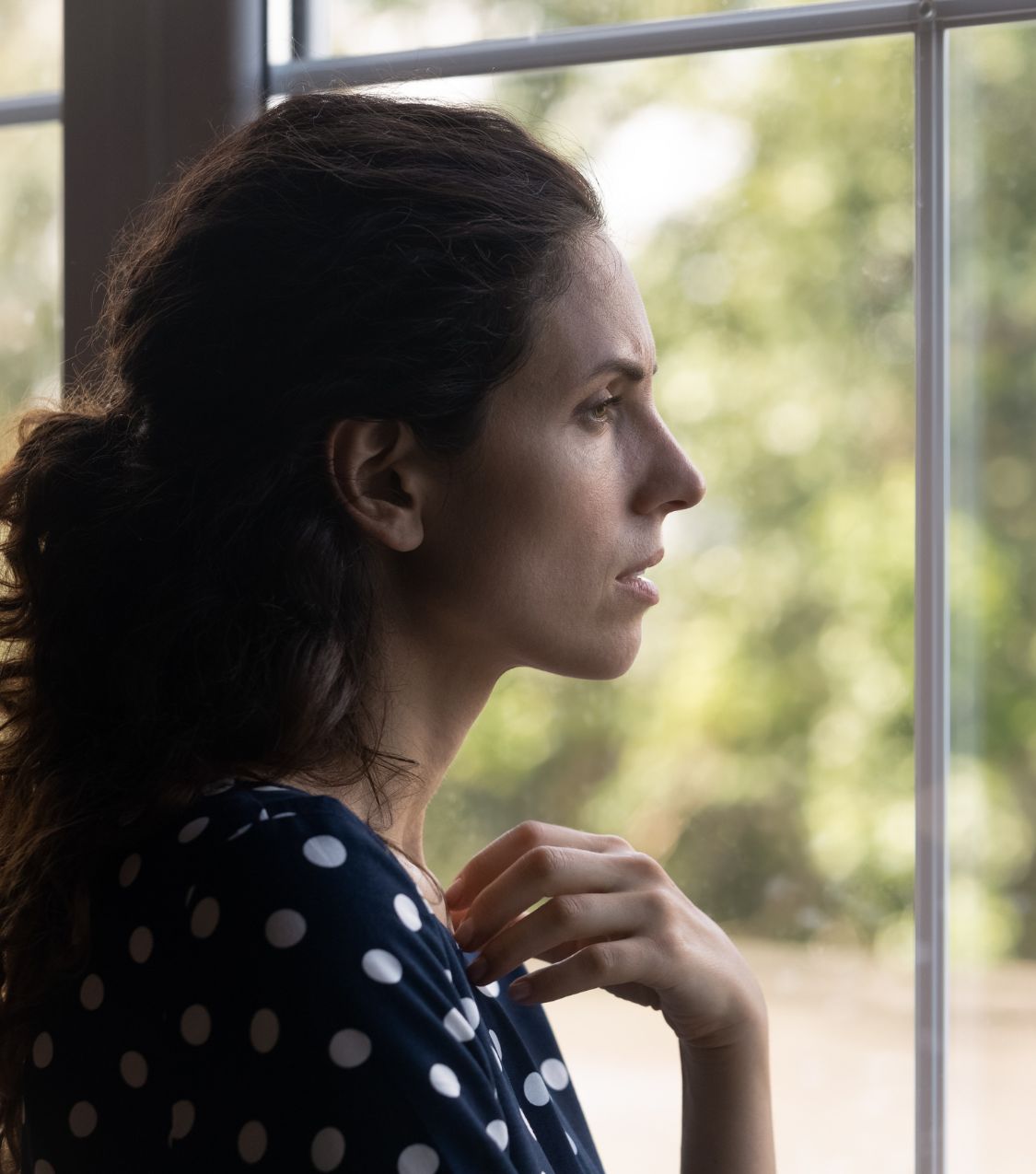 A woman looks out a window, deep in thought, reflecting on painful questions. Healing after a husband's affair with a man and a same-sex affair in a straight marriage. Book a confidential consultation with a licensed therapist in the USA, UK, or Canada.